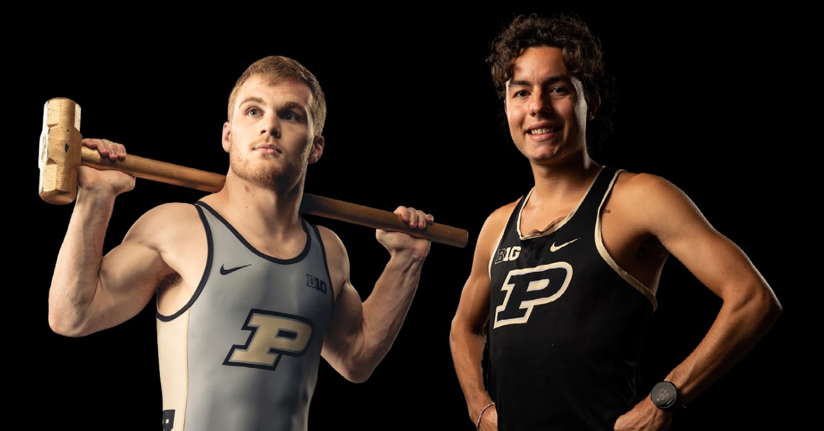 two athletes stand in front of a black background , on the left the male athlete has light hair and is holding a Purdue hammer on his shoulders, he is wearing a grey wresting suit. The male athlete on the right has dark hair and is standing with his hands on his hips, he is wearing a black track tank top.