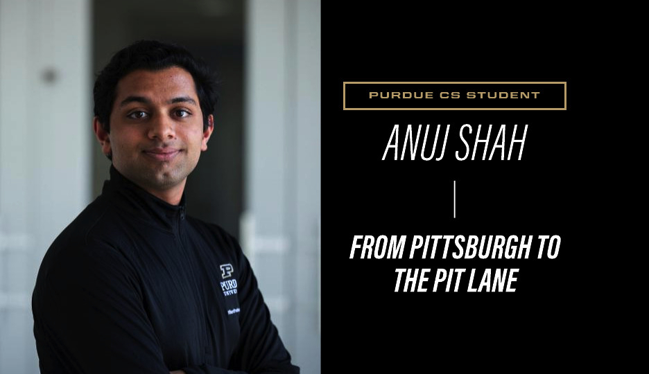 Anuj Shah in black Purdue quarter-zip jacket, arms crossed, smiling at camera against blurred indoor background.