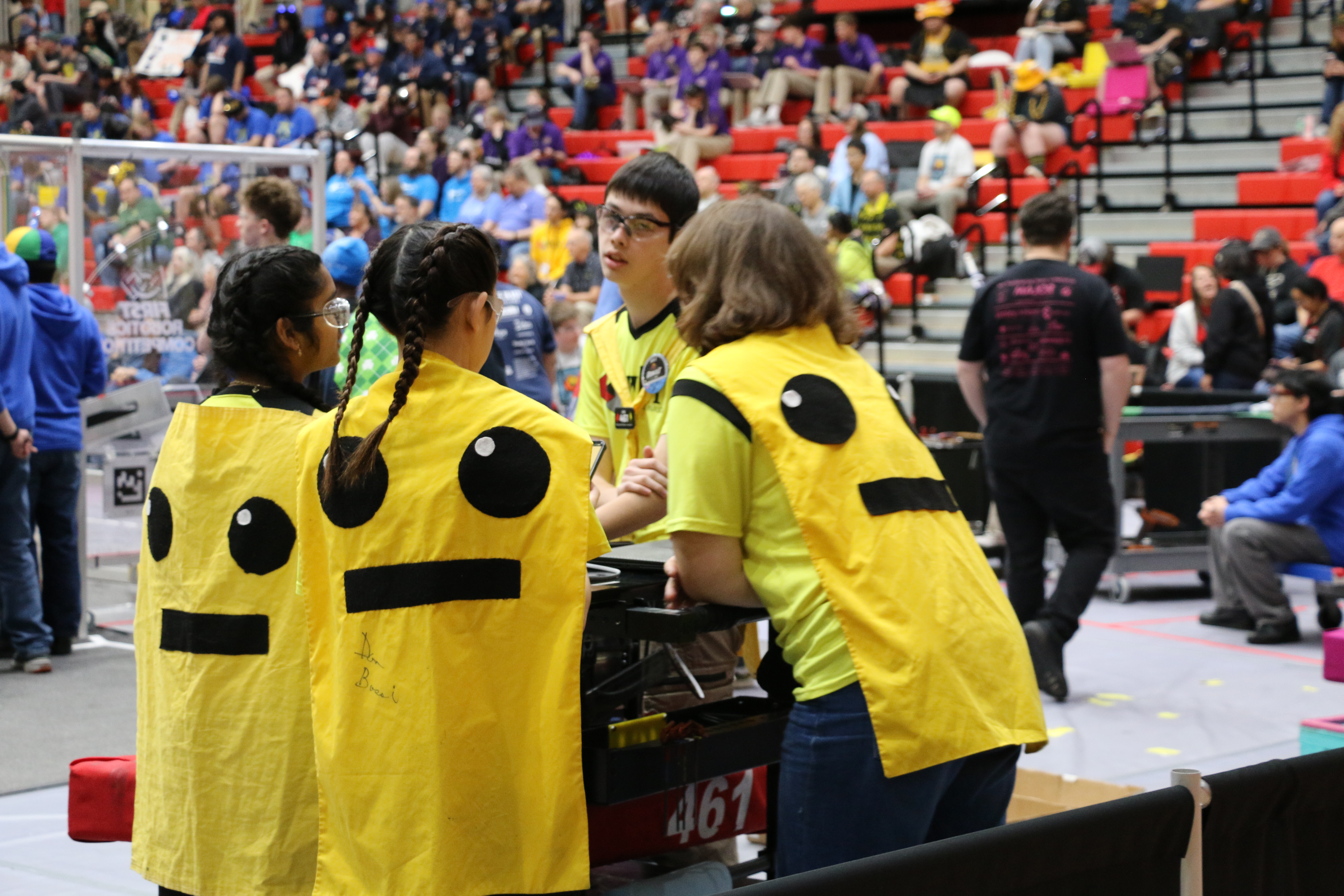 High school students in bright uniforms gather around their robot as they prepare to enter the competition field.